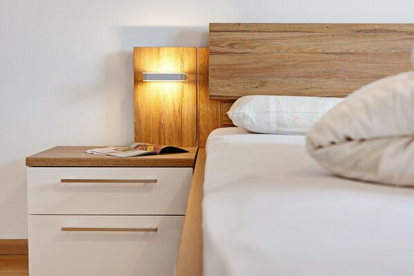Un dormitorio con cabecera de madera, mesita de noche con cajones, lámpara y cama con ropa blanca.
