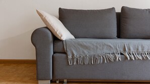 A grey sofa with a white pillow and a fringed throw blanket. - Apartment 'Klein' with Mountain View, Shared Garden and Wi-Fi (Velturno)