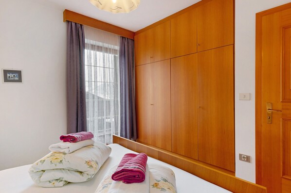 A hotel room with a bed, wooden wardrobe, and a window with curtains.