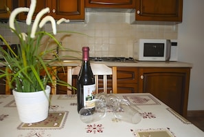 A kitchen with wooden cabinets, a microwave, a wine bottle, and wine glasses on a table.