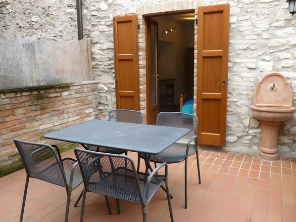 Un patio con una mesa, sillas, un muro de piedra y una puerta de madera.