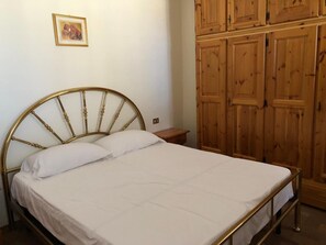 A bed with a gold headboard, a wooden nightstand, a wooden wardrobe, and a framed picture on the wall.