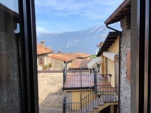 A view from a window overlooking a mountain, a courtyard with a staircase, and traditional buildings with tiled roofs.