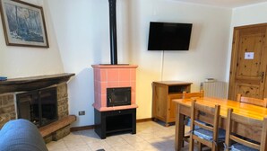 A living room with a fireplace, a television mounted on the wall, a dining table with chairs, and a wooden cabinet. - Apartment 'Casa Mary Castagno' with Wi-Fi (Prabione)