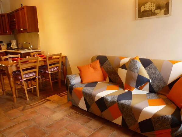 Una sala de estar acogedora con un sofá estampado, una mesa de comedor con sillas y una zona de cocina.