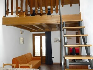 Un espacio tipo loft con techo alto, escalera de madera, sofá y zona de escritorio.