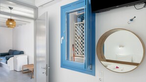 A room with a bed, a small table, a blue-framed window, a round mirror, and a television mounted on the wall. - Apartment 'Nicolas House 4' with Sea View, Wi-Fi and Air Conditioning (Rakhídhion)