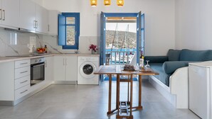 A modern kitchen with white cabinets, a built-in oven, and a washing machine. There is a wooden table with a view of the sea through an open door. - Apartment 'Nicolas House 4' with Sea View, Wi-Fi and Air Conditioning (Rakhídhion)