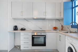 Une cuisine compacte avec des meubles blancs, un four encastré, un lave-linge et une machine à café.