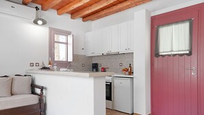 A compact kitchen with white cabinets, a red door, a wooden ceiling, and a small dining area with a bench. - Apartment 'Nicolas House 1' with Sea View, Wi-Fi and Air Conditioning (Rakhídhion)
