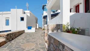 A narrow stone-paved street flanked by white buildings with blue accents, a stone wall, and a potted plant. - Apartment 'Nicolas House 2' with Sea View, Private Terrace and Air Conditioning (Rakhídhion)