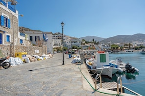 Un pueblo costero con edificios de piedra, un muelle con barcos y un cielo azul despejado.