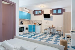Habitación de hotel pequeña con piso a cuadros, cama, kitchenette, comedor y televisor montado en la pared.