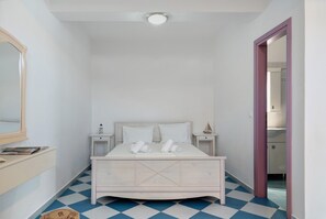 Quarto com cama, mesas de cabeceira, espelho e porta para outro cômodo.