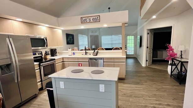 A modern kitchen with a central island, stainless steel appliances, and a 'let's eat' sign.