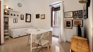 A compact living space with a dining table, chairs, a sofa, a bookshelf, a clock, and framed artwork on the walls. - Apartment 'Home Sweet Home' with Balcony, Wi-Fi and Air Conditioning (Giovinazzo)