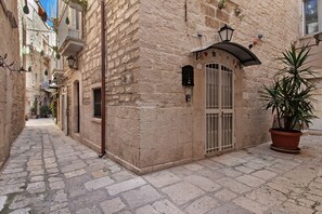 A narrow cobblestone street with stone buildings, a potted plant, and a metal gate.