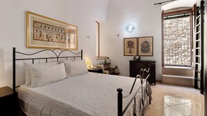 A bedroom with a bed, a nightstand, a wall-mounted picture, a window with a view, and a door. - Apartment 'Home Sweet Home' with Balcony, Wi-Fi and Air Conditioning (Giovinazzo)