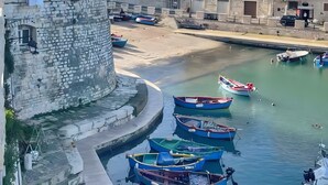 Un pueblo costero con edificios de piedra, una torre de piedra y barcos amarrados a lo largo del paseo marítimo.
