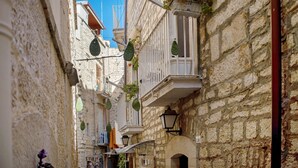 Una calle estrecha con edificios de piedra, balcones con plantas y faroles colgantes.