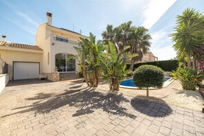Une maison avec une piscine, une terrasse dallée et diverses plantes tropicales.