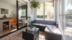 A sunlit room with a glass door leading to a balcony, wicker furniture, and a hanging plant.