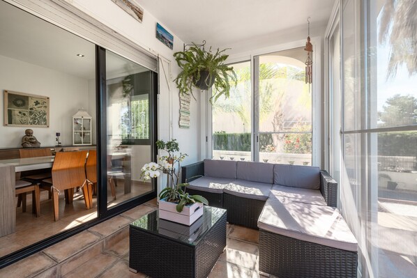 A sunlit room with a glass door leading to a balcony, wicker furniture, and a hanging plant.