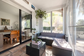 A sunlit room with a glass door leading to a balcony, wicker furniture, and a hanging plant.