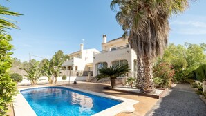 A swimming pool with a tiled deck, surrounded by palm trees and a building with a white facade.