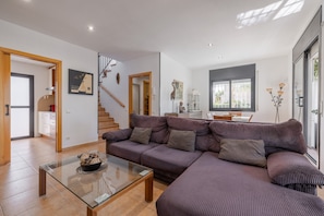 Un salon moderne avec un canapé d’angle, une table basse en verre et un escalier menant à l’étage supérieur.