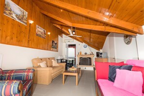 Un salon chaleureux avec un plafond en bois, une cheminée, un canapé, un fauteuil coloré et un téléviseur.
