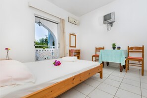 A bedroom with a bed, a TV, a table with chairs, and a window.