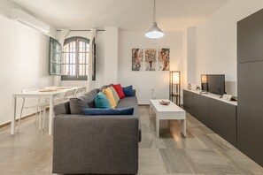 A modern living room with a sofa, a dining table, a TV, and artwork on the wall. - Apartment 'Tulip' Air Conditioning (Sevilla)