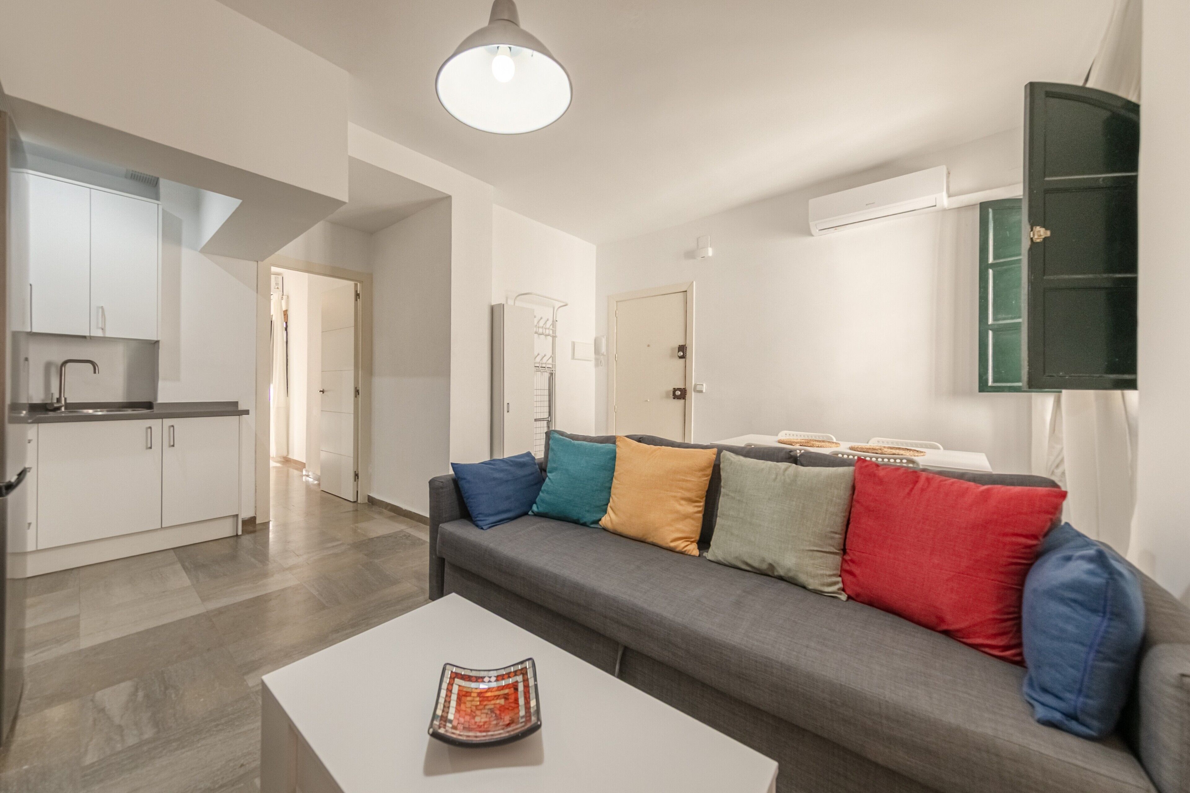 A modern living room with a grey sofa, a white coffee table, and a kitchen area in the background.