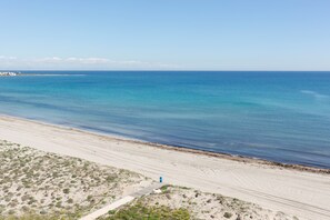 Uma praia com vista clara do oceano, um caminho de areia e vegetação esparsa.