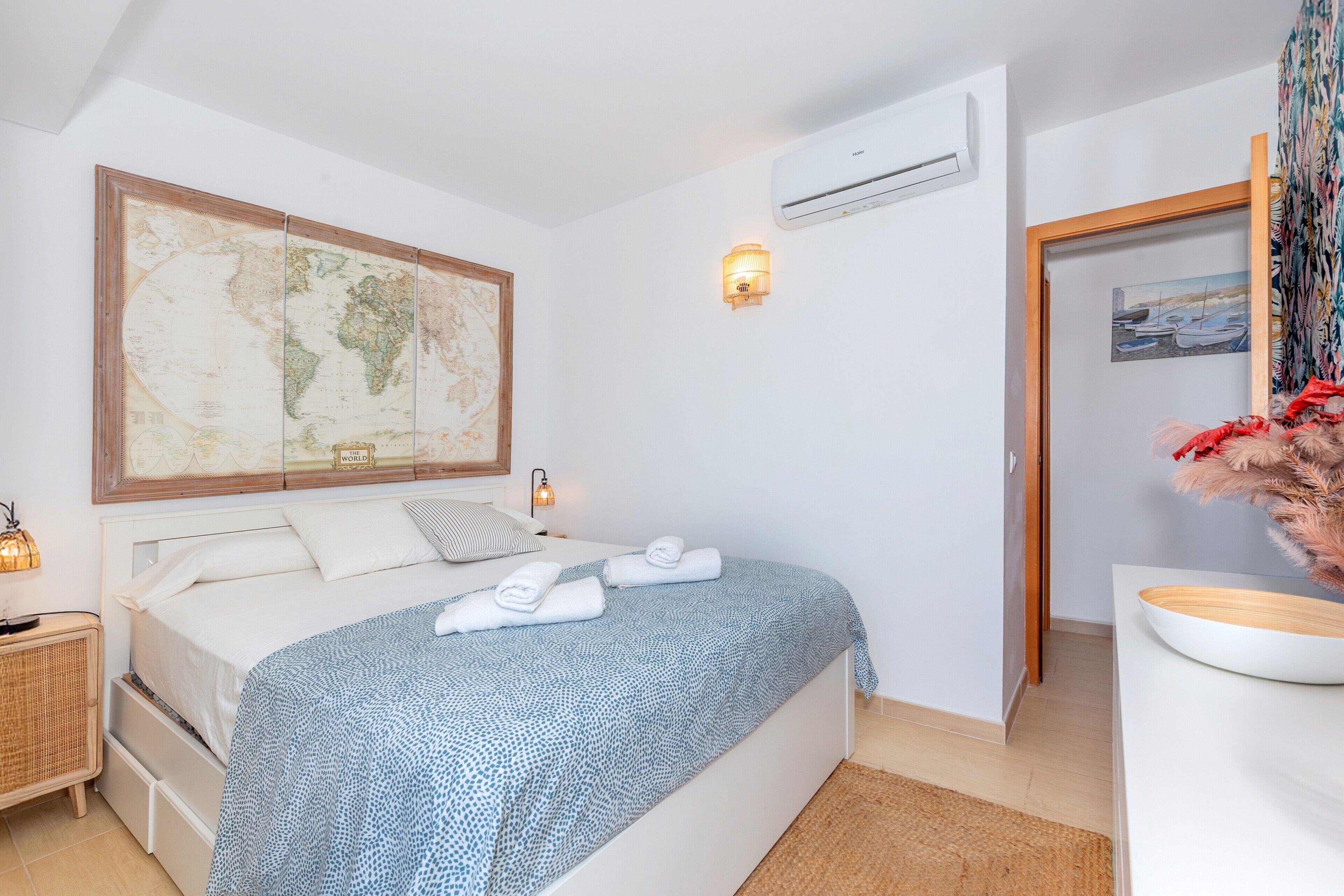 Et soveværelse med et stort verdenskort, en seng med hvide sengetøj, en senelampe og en aircondition.