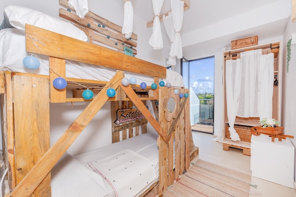 A bunk bed with a wooden frame, a small kitchen area, and a view through a glass door.
