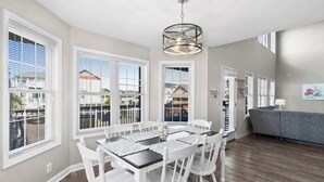 Uma sala de jantar com uma mesa posta para quatro pessoas, cadeiras brancas e um lustre.