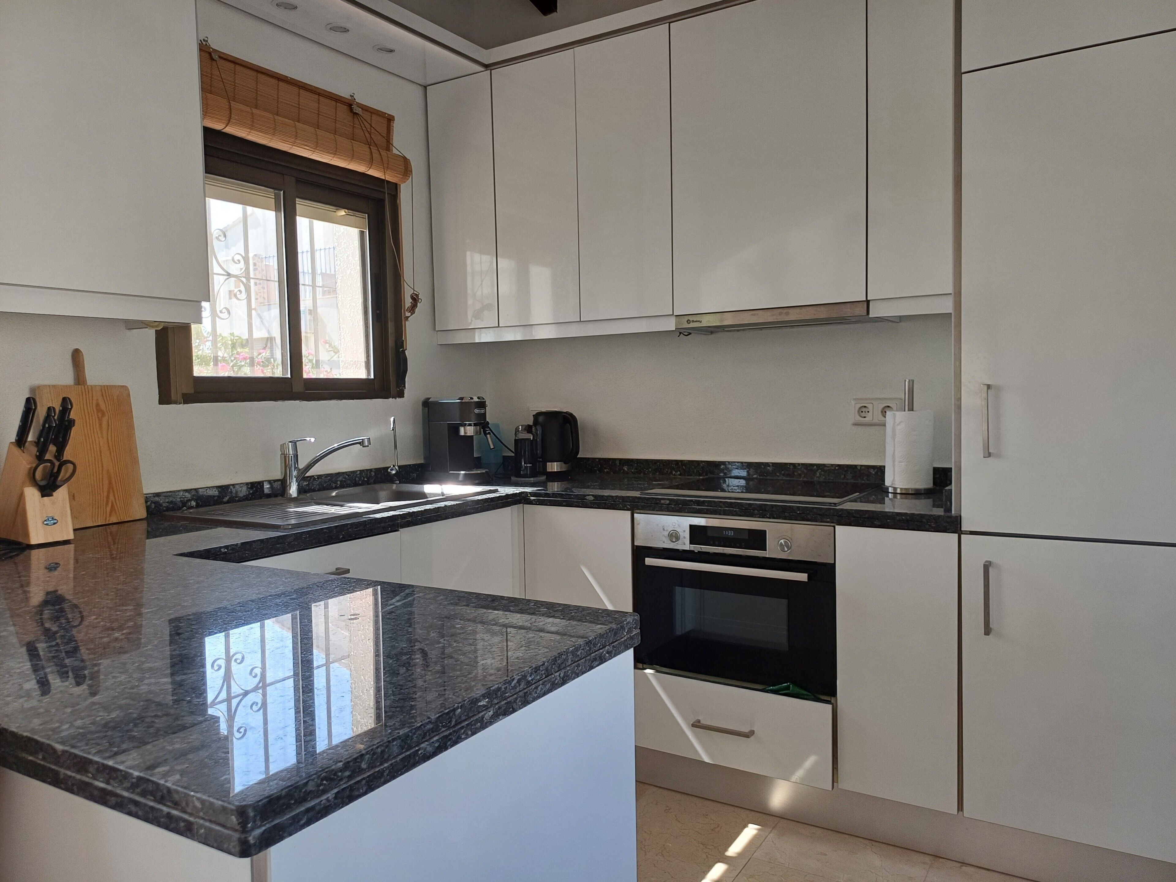A modern kitchen with white cabinets, a granite countertop, a coffee maker, and an oven.