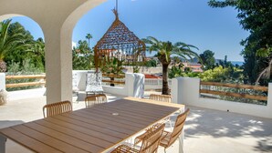 A wooden table with chairs, a hanging chair, and a view of the sea and greenery. - Villa 'Casa Mar Y' with Sea View, Wi-Fi and Air Conditioning (Moraira)
