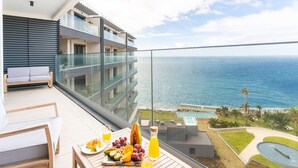 Ein Balkon mit Blick auf den Ozean, ein Tisch mit Früchten und Saft, und ein modernes Gebäude im Hintergrund.