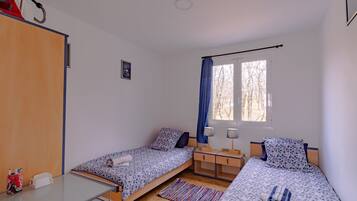 A room with two single beds, a desk, a chair, a wardrobe, and a window with curtains.
