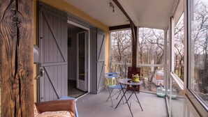 Varanda coberta com mesa e cadeiras, porta deslizante e vista para árvores e uma casa rodante lá fora.