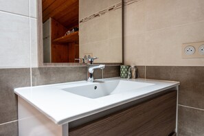 Un baño con lavamanos blanco, tocador de madera y un espejo.