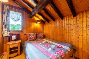 A wooden-paneled room with a bed, a nightstand, a window with curtains, and a lamp.