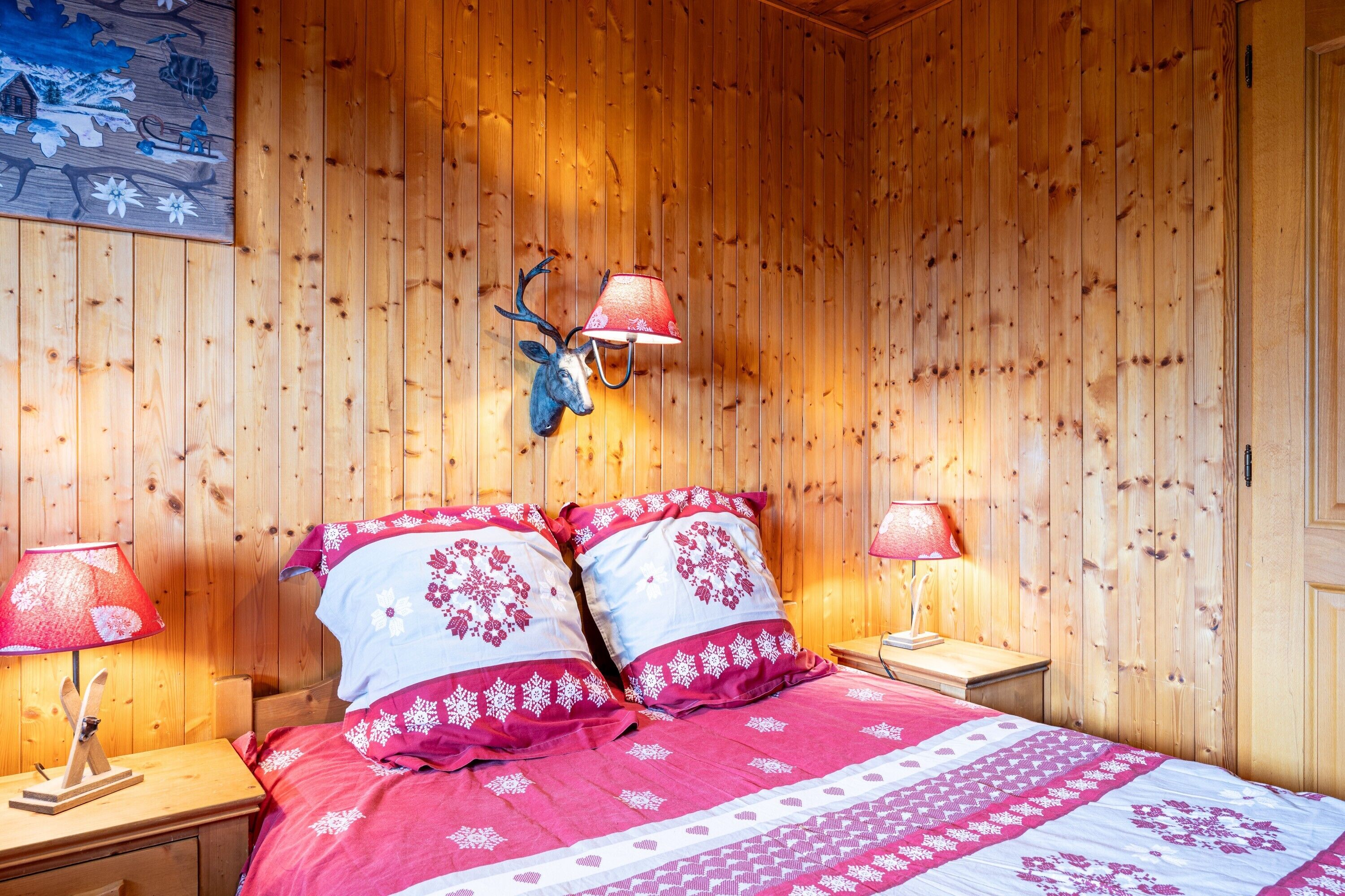 A wooden-paneled room with a bed, two bedside lamps, and a deer head wall decoration.
