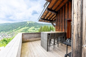 Una terraza de madera con mesa y sillas, con vistas a un paisaje montañoso.