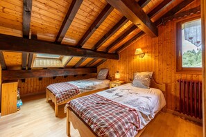 Une chambre dans une cabane en bois, avec deux lits, une lucarne, une fenêtre donnant sur un beau paysage et un plancher en bois.