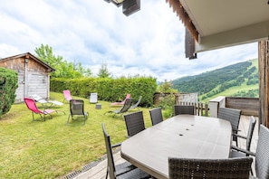 A patio with a table and chairs, a wooden shed, and a view of a green landscape.