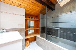 A modern bathroom with a wooden ceiling, a glass shower enclosure, a white sink, and a built-in shelf.